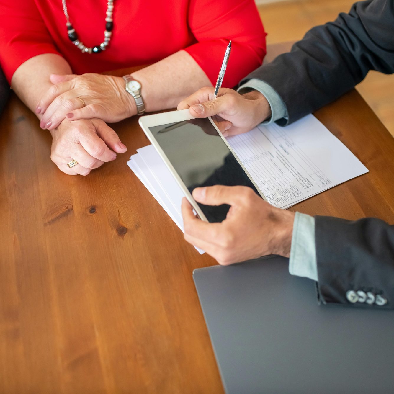 Zwei Personen besprechen Unterlagen an einem Tisch, eine hält ein Tablet.