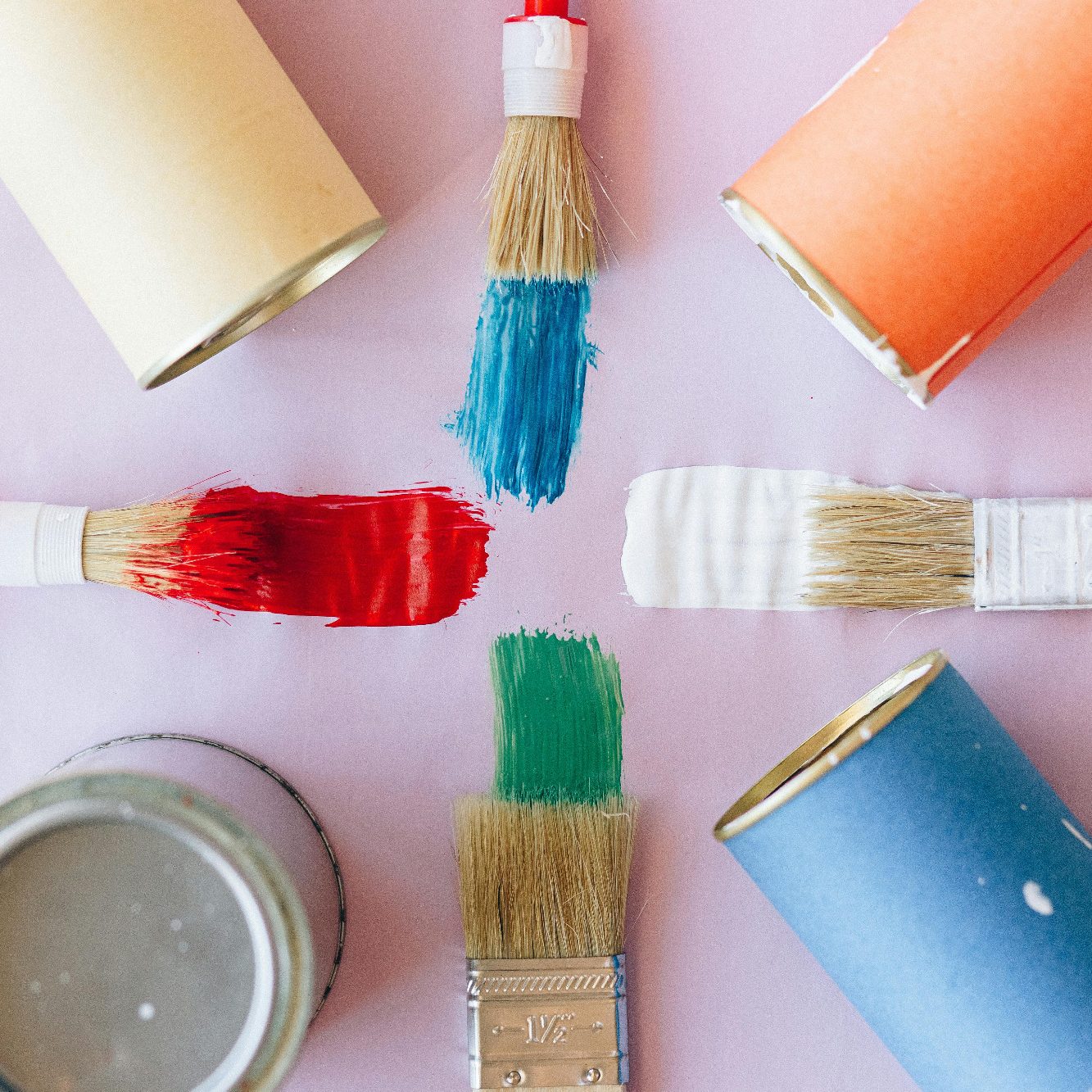 Bunt bemalte Pinsel und Farbtöpfe auf einer lila Unterlage angeordnet.