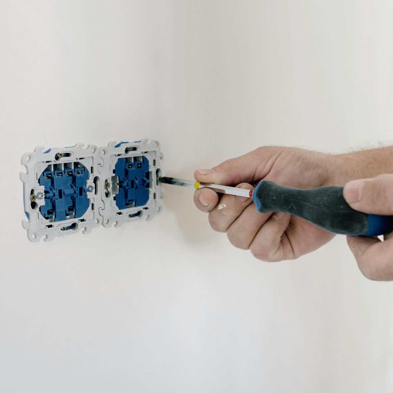 Hand hält einen Schraubenzieher, während ein elektrischer Anschluss an einer Wand bearbeitet wird.