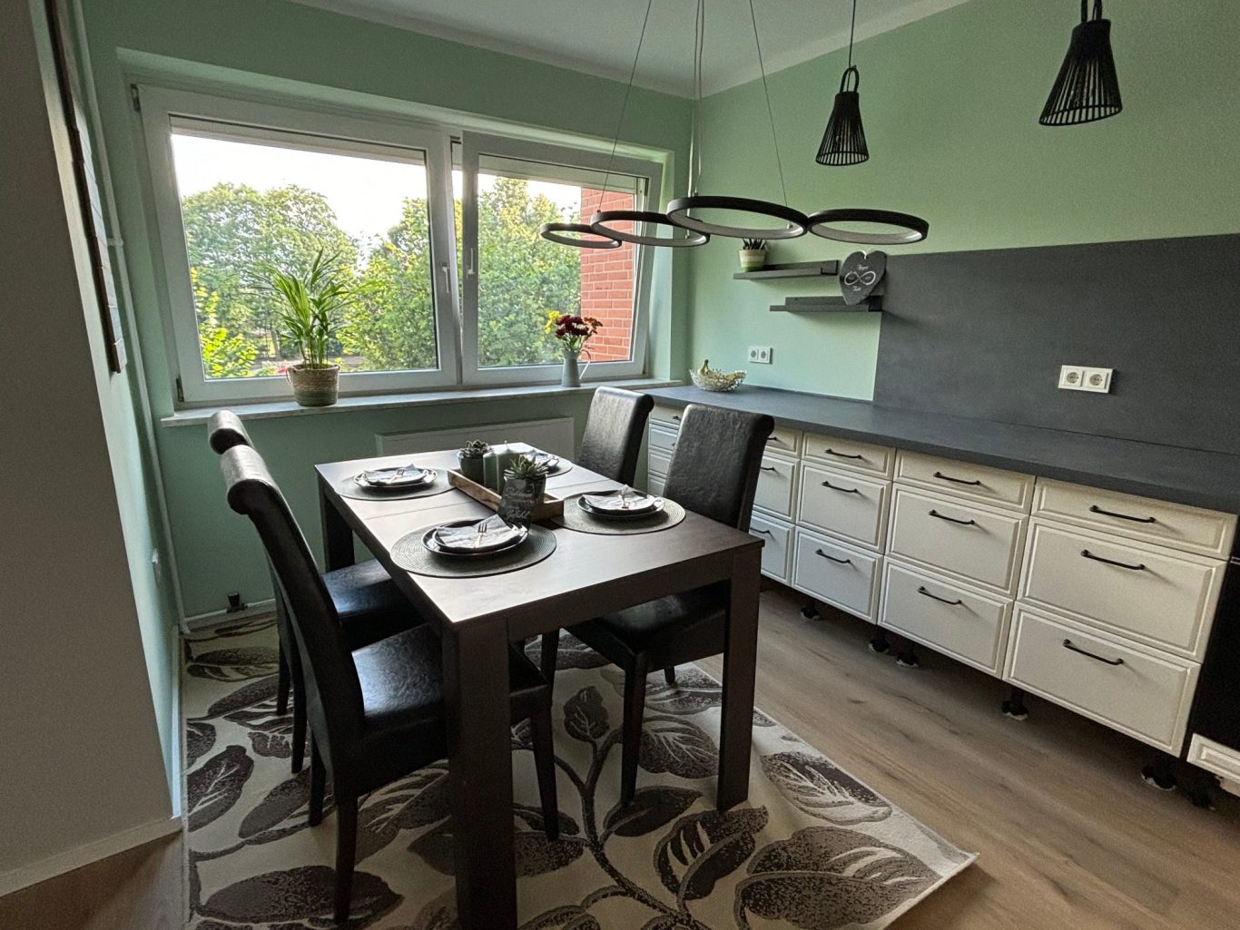 Moderne Küche mit Esstisch, Stühlen und Blick auf den Garten durch große Fenster.