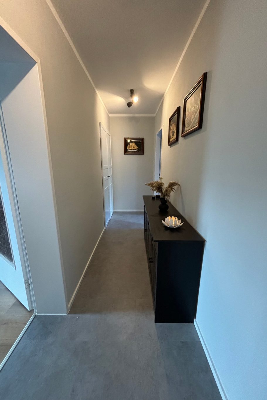 Heller Flur mit grauem Boden und schwarzem Sideboard, Bilder an den Wänden.