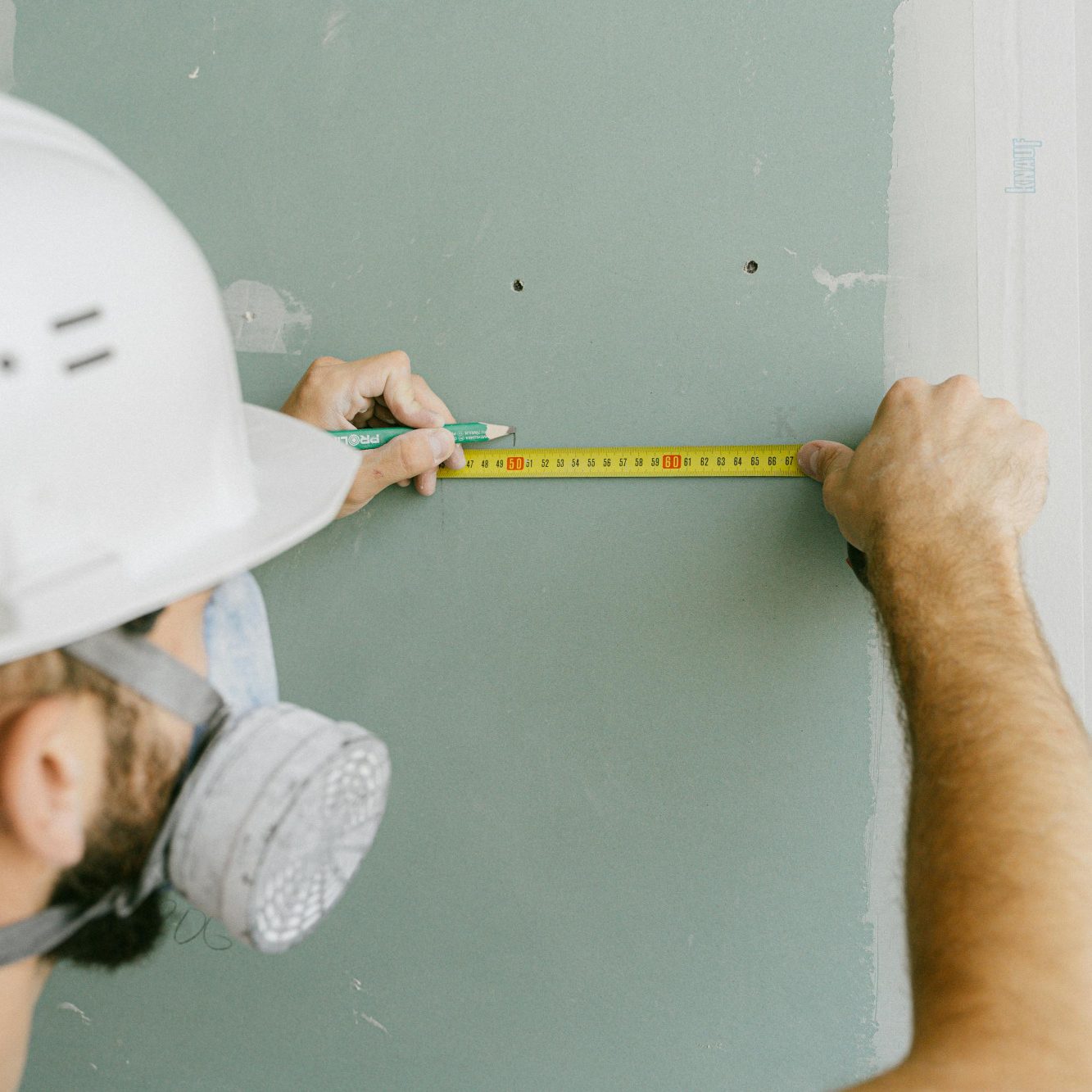 Ein Handwerker misst mit einem Metermaß eine Wand mit grauer Farbe.