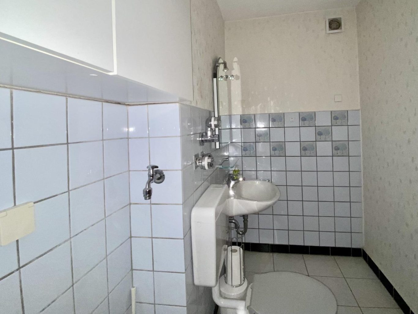 Kleines Badezimmer mit Waschbecken, WC und hellblauen Fliesen.