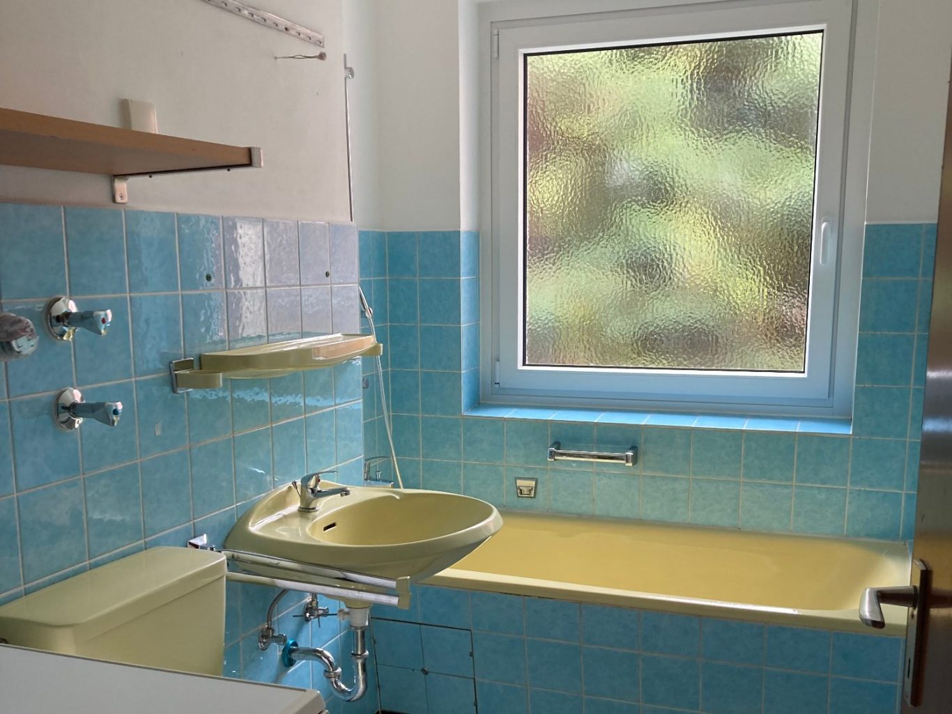 Badezimmer mit blauen Fliesen, gelber Badewanne und Fenster.
