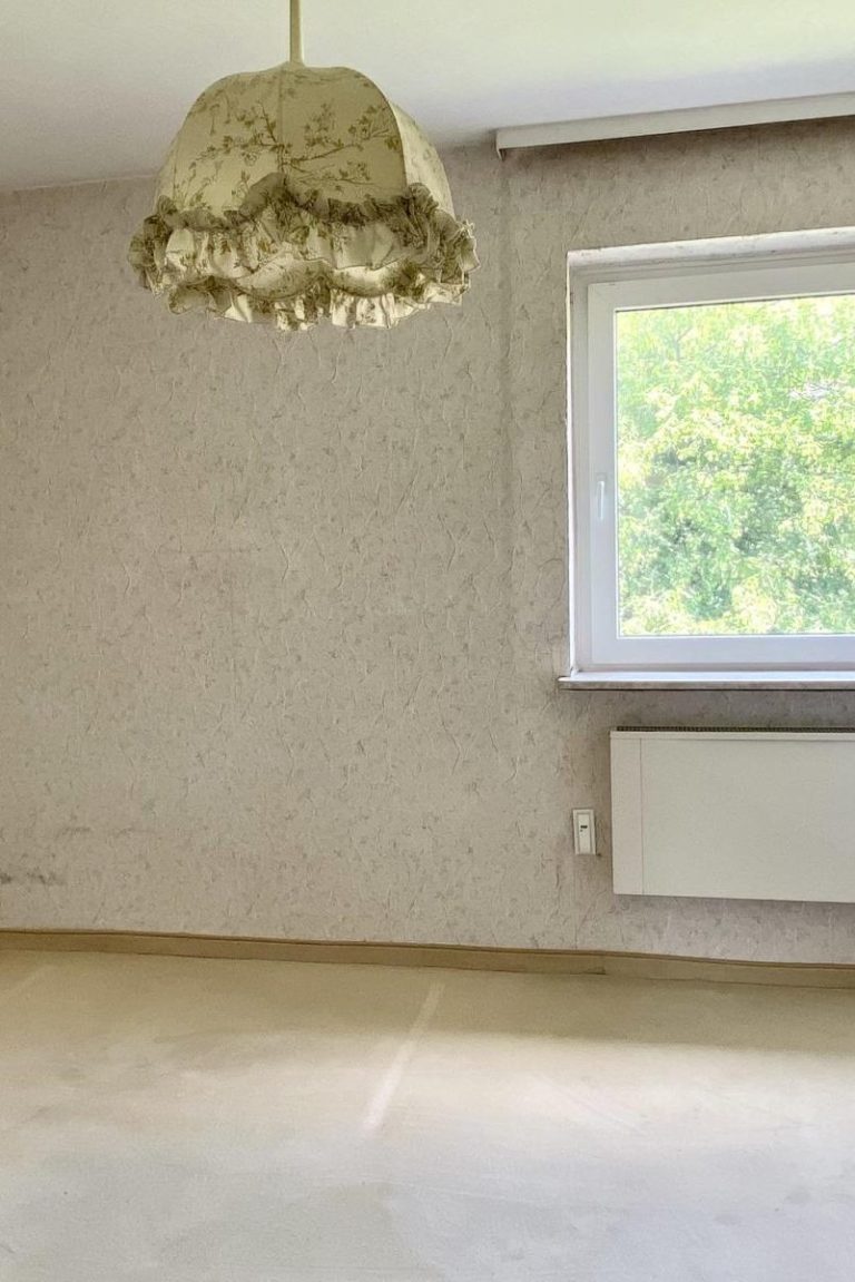 Leerer Raum mit einem Fenster, einer Heizung und einem 60er-Jahre-Lampenschirm.